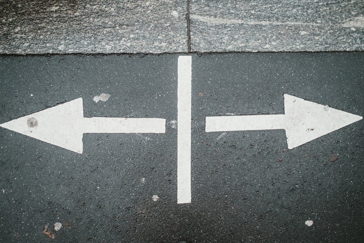Two white arrows pointing in opposite directions on asphalt, representing a decision point